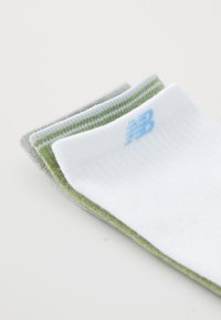 Tres pares de calcetines: uno blanco con un logo azul claro, uno gris y uno verde con rayas en la parte superior. Hechos de un tejido suave y texturizado.