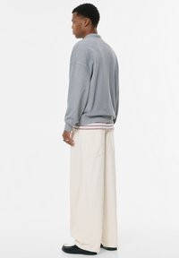 Grå sweatshirt med rund hals og ribbede manchetter, parret med løstsiddende, cremefarvede bukser og sorte sko. Enkel, afslappet pasform.