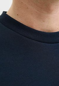 Nahaufnahme des Nackens einer Person und des gerippten Kragens eines dunkelblauen Strickpullis.