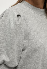 Grå sweatshirt tillverkad av mjukt material, med rundad ringning och puffiga axelpartier för extra textur.