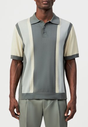 Mann trägt kurzärmeliges Poloshirt mit vertikalen Streifen in Grautönen, Creme und Beige, kombiniert mit grauer Hose.