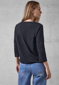 Schwarzes Langarmshirt mit lockerer Passform, ausgestattet mit einem weit ausgeschnittenen Halsausschnitt, kombiniert mit hellblauen Jeans aus Denim mit normalen Gesäßtaschen.