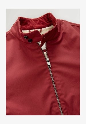 Burgundijska jakna s stoječim ovratnikom, z zadrgo na sp rednji strani, dvema črnima gumboma in mehkim kremnim notranjim podloženjem.