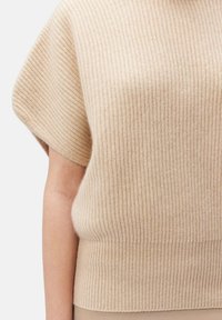 Beige ribbad stickad topp med korta dolmansärmar, med en mjuk textur och en åtsittande nederkant. Enkel, ren design.