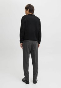 Suéter negro con cuello redondo y tejido texturizado. Combinado con pantalones grises de corte holgado que tienen dos bolsillos traseros y un patrón sutil.