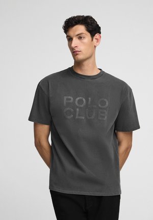 Camiseta de algodón gris carbón con un estampado tonal de "POLO CLUB". Corte relajado con cuello redondo y mangas cortas. Textura suave.