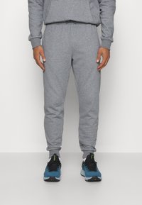 Graue Sweatpants aus weichem Baumwollmaterial, mit schmal zulaufendem Beinschnitt und elastischem Bund, kombiniert mit blauen Sportschuhen.