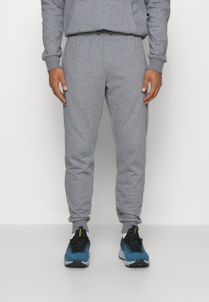 Graue Sweatpants aus weichem Baumwollmaterial, mit schmal zulaufendem Beinschnitt und elastischem Bund, kombiniert mit blauen Sportschuhen.