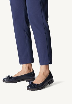 Ballerines en cuir verni bleu marine avec un accent en nœud, bout arrondi et semelle texturée, associées à un pantalon bleu marine ajusté.