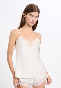 Jedwabny kremowy top na cienkich regulowanych ramiączkach z koronkowym wykończeniem przy dekolcie, w zestawie z pasującymi szortami ozdobionymi koronką.
