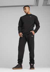 Sweatshirt și pantaloni sport negri din material moale, cu glugă și logo. Pantalonii au buzunare și o croială conică.