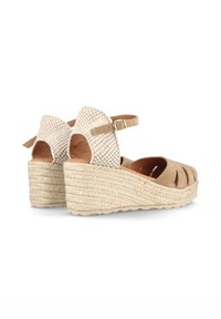 Sandalias de cuña beige con tacón de tela trenzada, diseño de punta descubierta, correa ajustable en el tobillo y plataforma de yute texturizado.