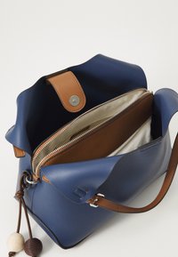 Sac en cuir bleu avec un rabat en cuir marron, fermeture éclair dorée et poche intérieure. Présente des perles décoratives beiges et marron sur le cordon de serrage.