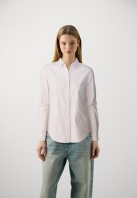 Chemise boutonnière rose clair avec un col rond et des manches longues, associée à un jean bleu clair, ample et décontracté. Design minimaliste.