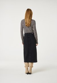 Schwarzer Denim-Maxikleid mit schmaler Taille und Gesäßtaschen, kombiniert mit einem Langarmtop, das ein weißes gepunktetes Muster auf dunklem Hintergrund zeigt.