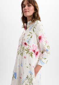 Leinenkleid mit Blumenmuster in den Farben Pink, Blau und Grün, einem knöpfbaren Kragen und langen Ärmeln mit hochrollbaren Manschetten.