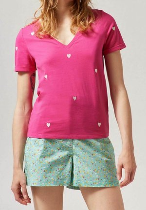 Femme portant un t-shirt rose à col en V avec de petits cœurs blancs et un short bleu clair à petit motif floral.