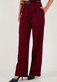 Pantaloni largi de culoare bordeaux, confectionati dintr-un material neted, avand talie inalta, pliuri frontale si buzunare laterale, asortati cu un cureaua neagra si tocuri ascutite.