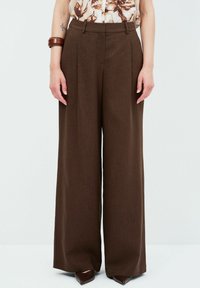 Bruine, wijde broek met een gestructureerde afwerking en voorplooien. Hoge taille ontwerp gecombineerd met puntige schoenen.