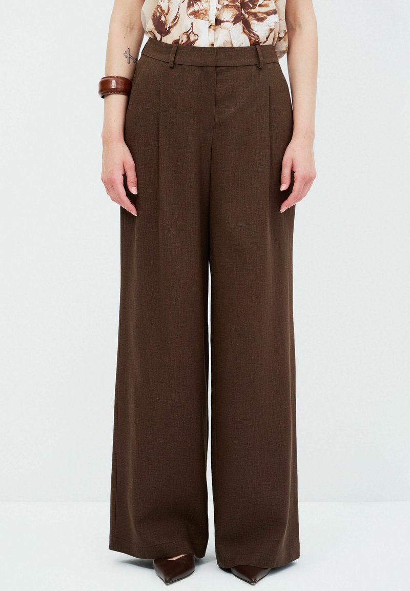 Bruine, wijde broek met een gestructureerde afwerking en voorplooien. Hoge taille ontwerp gecombineerd met puntige schoenen.