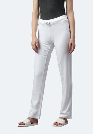 Weiße Baumwoll-Jogginghosen mit einem elastischen Bund und Kordelzug, die einen lockeren Schnitt und eine glatte Textur aufweisen. Kombiniert mit flachen Sandalen.