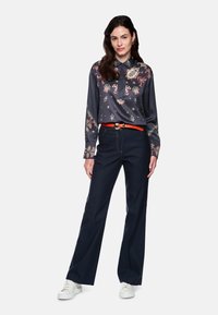 Dark gray long-sleeve blouse with colorful floral patterns, paired with navy wide-leg trousers and white sneakers, featuring an orange belt.