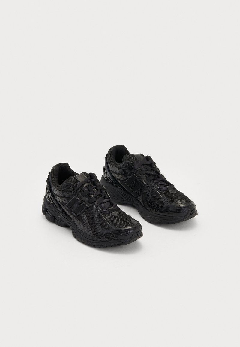 Paire de baskets noires avec des panneaux en mesh, des semelles épaisses et des lacets, inclinées pour montrer les chaussures gauche et droite sur un fond clair.