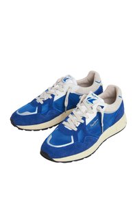 Modré športové tenisky vyrobené z semišu a sieťoviny, s krémovou gumovou podrážkou a bielymi šnúrkami. Obsahujú akcenty loga na jazyku.