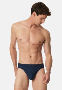 Marineblaue Badehose mit ribbed Struktur, mit einem niedrigen Bund und subtiler Markierung am Bund. Maßgeschneiderter Sitz für Komfort.