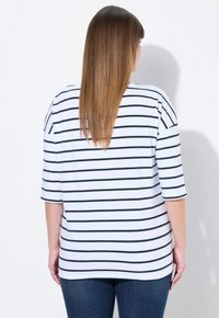 Weiß-blau gestreiftes kurzärmliges Shirt mit lockerer Passform, abgerundetem Saum und weichem Stoff. Kombiniert mit dunklen Jeans.