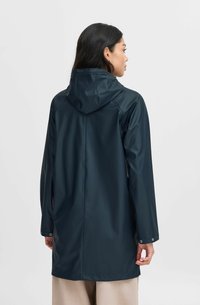 Pardoseală de apă de culoare verde închis, cu glugă, mâneci lungi și capse la manșete. Textură netedă și lucioasă, design până la genunchi.