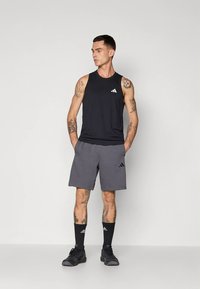 Μαύρο αμάνικο αθλητικό τοπ και γκρι σορτς, και τα δύο με το λογότυπο της Adidas. Το ντύσιμο διαθέτει αναπνεύσιμο ύφασμα και άνετη εφαρμογή.