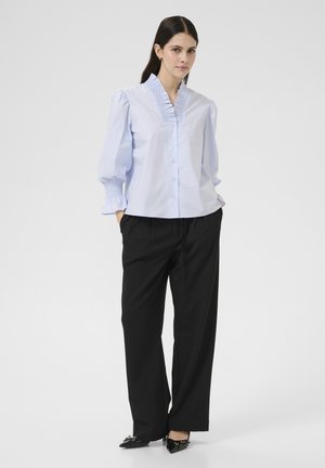 Lichtblauwe, met kraag, blouse met ruches, lange pofmouwen en knoopsluiting; gecombineerd met hoge, zwarte broeken.