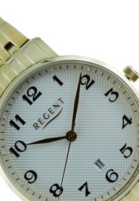 Montre dorée avec un cadran blanc texturé, des chiffres et des aiguilles noirs. Présente une fenêtre de date à 6 heures, maintenue par un bracelet en métal.