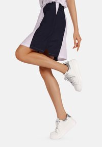 Sneakers bianchi con dettagli argentati, tomaia in pelle liscia e suola spessa abbinati a una gonna navy e rosa, che mostrano un outfit casual.