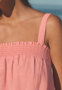 Ljusrosa ärmlös blus med smockad överdel, mjuk textur och lätt fall, perfekt för varmt väder.