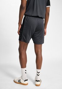 Svarta atletshorts med vertikala småränder, kombinerade med vita och svarta sneakers samt vita strumpor med svarta chevronmönster.