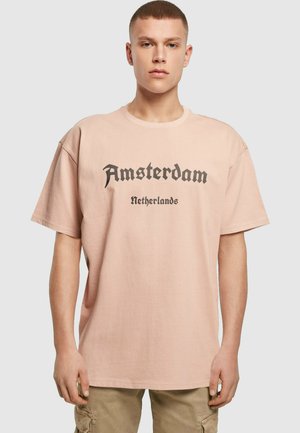 Light pink oversized t-shirt made of cotton, featuring bold black text that reads "Amsterdam Netherlands," short sleeves, and a round neckline.