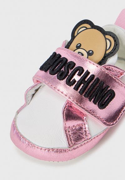 Ružová metalická topánka pre malé deti s čiernym popruh s nápisom "Moschino" a aplikáciou medvedíka. Vyrobená z plastových materiálov s textúrovaným povrchom.