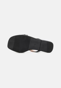Semelle de sandale noire avec une surface en caoutchouc texturée ; comprend un design large et plat et un léger talon. Présente un branding minimal et aucun accent notable.