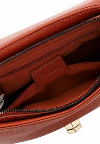 Interior de un bolso de piel texturizada roja con un bolsillo con cremallera, forro suave y un toque de metal en tono dorado.
