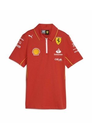 Czerwona koszulka polo z żółtymi akcentami; posiada zamek błyskawiczny przy kołnierzy oraz wiele logo, w tym Ferrari, Shell i Puma, na przodzie i rękawach.