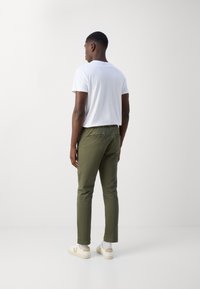 Tricou alb cu mânecă scurtă, pantaloni conici în nuanță de verde măsliniu și adidași bej cu logo. Textură de bumbac neted, croială lejeră.