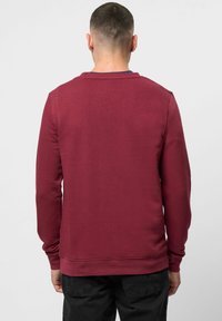 Burgunderfarget genser med lange ermer, rund hals og ribbestrikkede mansjetter. Glatt tekstur, minimalistisk design, og ingen synlige logoer.