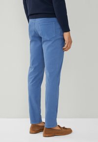 Pantalones de algodón azul claro con corte slim, que cuentan con dos bolsillos traseros y una textura suave, combinados con mocasines de ante marrón.