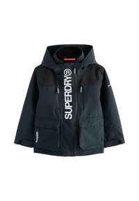 Giacca a vento Navy con pannelli superiori neri, grande logo frontale, multiple tasche con zip e patta, cappuccio regolabile e polsini elasticizzati.