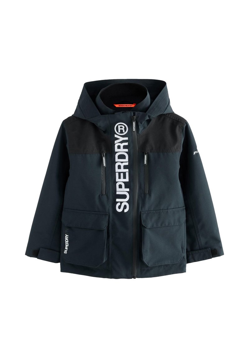 Giacca a vento Navy con pannelli superiori neri, grande logo frontale, multiple tasche con zip e patta, cappuccio regolabile e polsini elasticizzati.