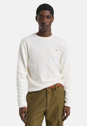 Witte sweatshirt van zachte stof met een ronde hals en lange mouwen, met een klein logo-detail op de borst, gecombineerd met olijfgroene broeken.