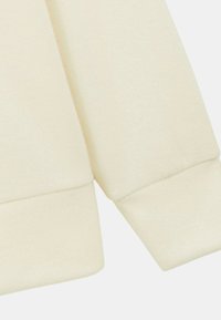 Poignet de sweatshirt couleur crème avec texture côtelée et détail de couture, mettant en avant un matériau doux semblable au coton. Design épuré et simple.