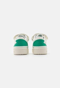 Gröna och vita sneakers med texturerade gröna detaljer, en slät vit sula och platta snören. Bakifrån visas hälflikarna och sömnadsdetaljer.